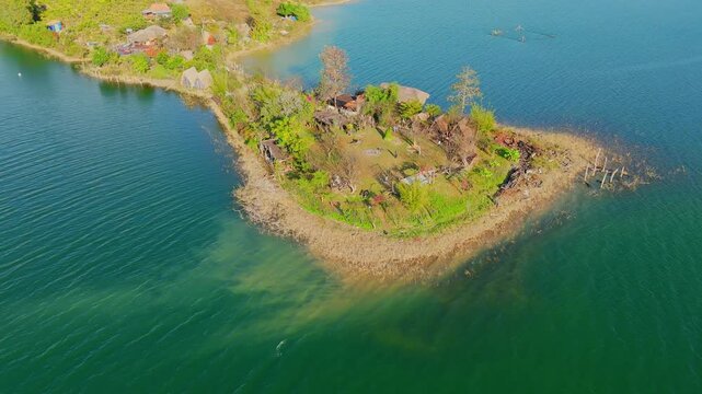 Aerial drone view of Hon Mong Tay island in Phu Quoc showing small rocky land, rustic huts, clear turquoise water, and surrounding shoreline creating peaceful tropical scene