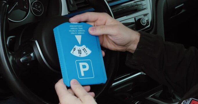 Close-up of a person setting a parking disc inside a car. Concept of parking regulation, time control and driving routine.