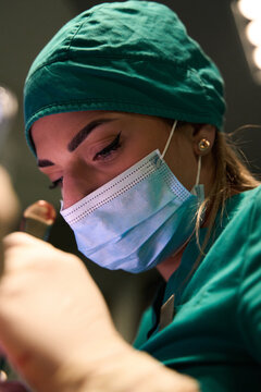 Female surgeon focused during delicate surgery in an operating room wearing mask and scrubs