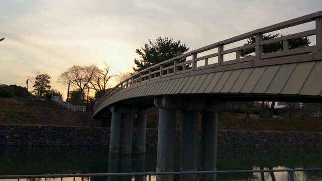 A serene panning shot of the historic Uji Wooden Bridge, also known as Asagiri Bridge, over the tranquil Uji River in Uji, Japan. The camera slowly pans across the picturesque scene, capturing the nat