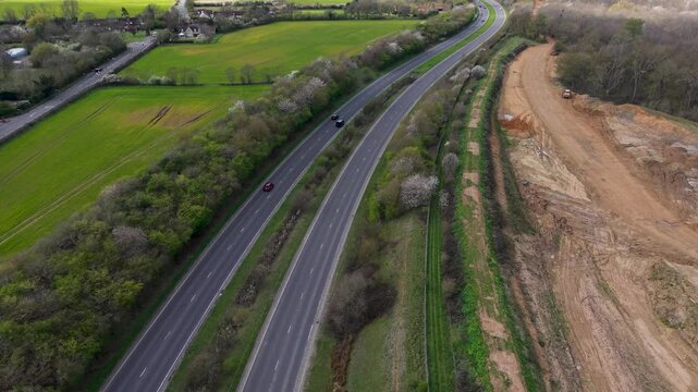 A414 reverse drone flight reveals Panshanger quarry beside dual carriageway, showing cars, farmland and woodland in Hertfordshire, England. Smooth pullback aerial for travel and infrastructure.