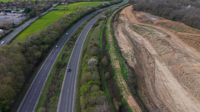 A414 road drone flight from Hertford to Hatfield, England, with Panshanger quarry to the right. Forward aerial tracking over cars, woodland edge and excavated landscape.