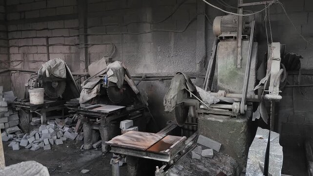 Inside a heavily dust-coated stone cutting workshop, large circular saws and masonry machinery sit idle. The thick layer of silica dust covering the equipment and floor