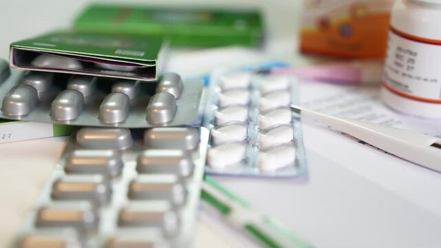 Blister packs of pills, thermometer and medication bottles on a white surface, shallow depth of field focusing on tablets