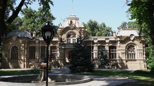 Tashkent (Toshkent), Uzbekistan (O'zbekiston) - May 26, 2025: The historic Prince Romanov Palace surrounded by lush green trees and a stone fountain in the park on a sunny day.