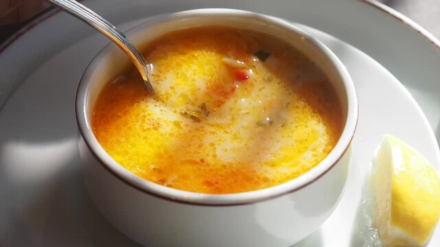 Creamy seafood soup being stirred with silver spoon in white bowl with fresh lemon garnish.