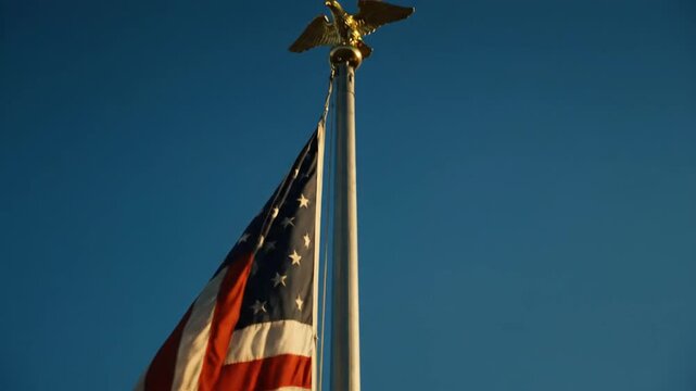 A worn and frayed American flag waving gracefully against a clear deep blue sky during sunset, captured in a close-up cinematic shot