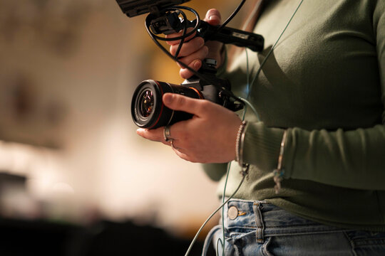 A person holds a camera with a microphone attached, preparing to film.