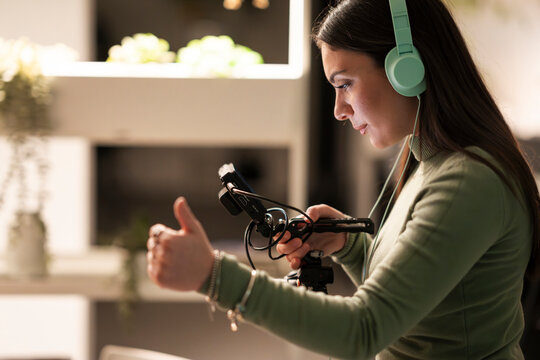 A young woman wearing headphones and a green sweater holds a camera rig and gives a thumbs up.