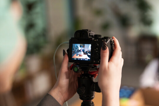 A person films a woman on a laptop screen, capturing content for a video or online presentation.