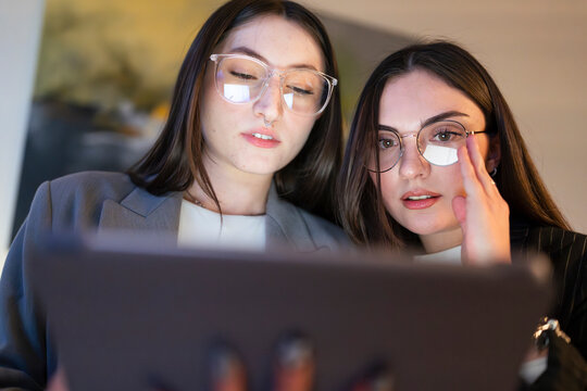 Two young women wearing glasses focus intently on a tablet screen, engaged in a collaborative task or discussion.