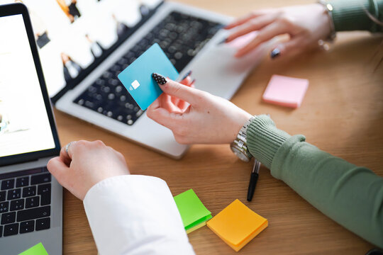 A person holds a credit card over a laptop, preparing to make an online purchase. Multiple sticky notes and a pen are on the desk.