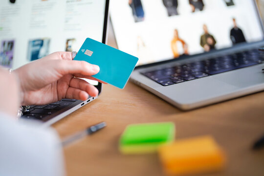 A person holds a credit card near a laptop, suggesting online shopping or a financial transaction.
