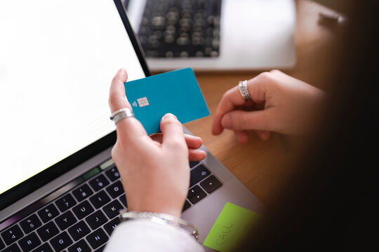A person holds a credit card over a laptop, ready to make an online purchase. The screen displays product listings and pricing information.