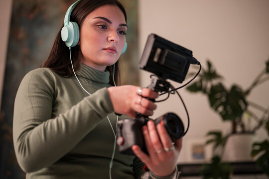 A young woman wearing headphones operates a camera with a monitor attached, focusing on her creative work.