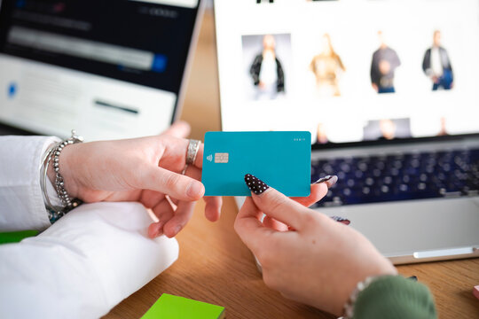 A person holds a debit card in front of a laptop displaying an online shopping website.