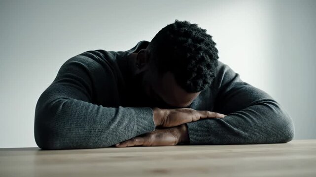 Man Sitting at Table with Head Down in Despair.