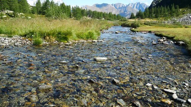 Calm transparent waters of a mountain torrent at the famous Arpy Lake, Aosta Valley, Italy. Natural landscape with high peaks of italian alps on the background, with blue sky