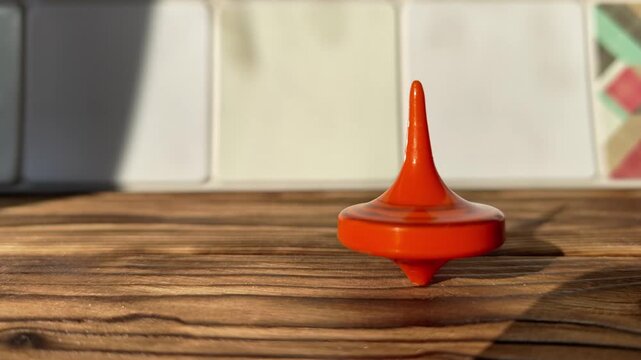 Orange spinning top balances and turns on wood as light shines in.