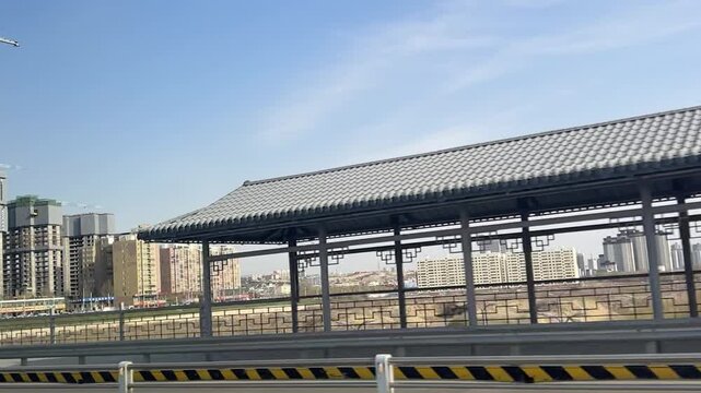 Low angle wide shot of an empty modern bus stop or outdoor shelter with a tiled roof and a city skyline in the background.