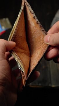 Close-up of hands opening a leather wallet, revealing its interior compartments and zipper details against a dark wooden background