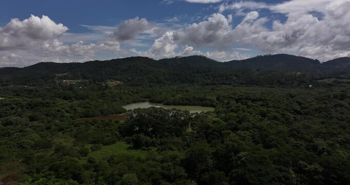 4K drone view of Leon Feffer Park in Mogi das Cruzes, Brazil, showing forest, lake and urban surroundings under blue sky and clouds.