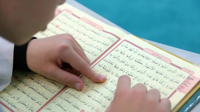 Close up of a hand following the verses of the Quran with a finger during a religious lesson for tajweed and pronunciation at an islamic school or mosque for young students