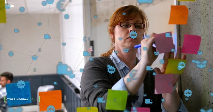 Animation of connected icons over caucasian businesswoman writing on sticky note on glass wall