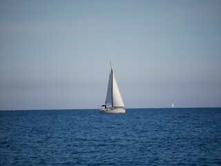 Fototapeta premium Sailboat gliding across the calm blue ocean under a clear sky, creating a minimalist and serene seascape in Barcelona, Spain