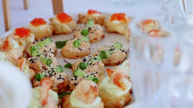 Refined appetizer plate featuring delicate canapes with salmon, cucumber, shrimp, sesame seeds, red caviar beside sparkling crystal glasses, presenting gourmet culinary presentation