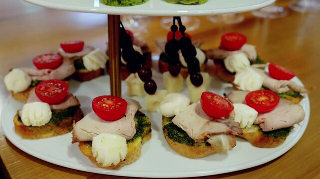 Gourmet canapes with cherry tomatoes, cream cheese, pesto garnishing crispy toasted bread, elegantly displayed on white multi level serving platter