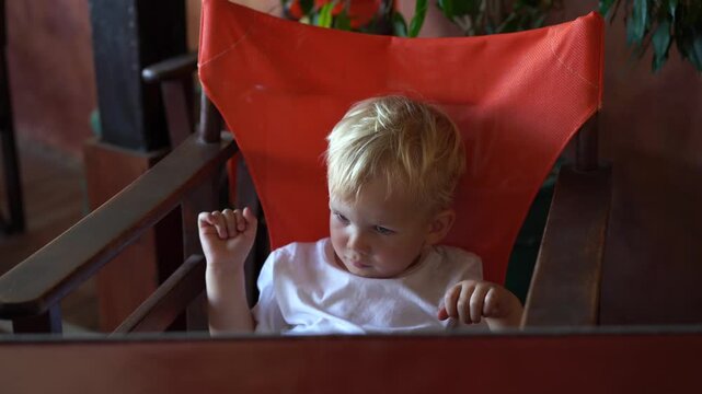 Excited toddler boy waiting for food plays with his feet and happily slaps the restaurant table in anticipation.