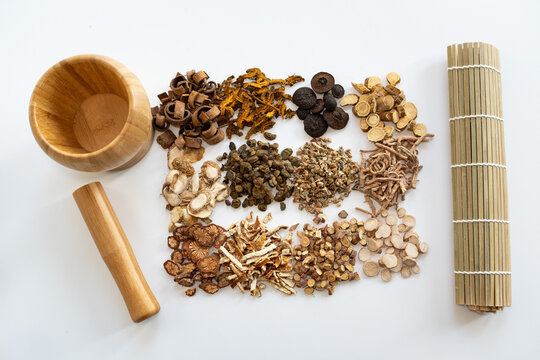 Traditional Chinese medicine decoction pieces arranged with wooden mortar pestle and bamboo scroll on white background