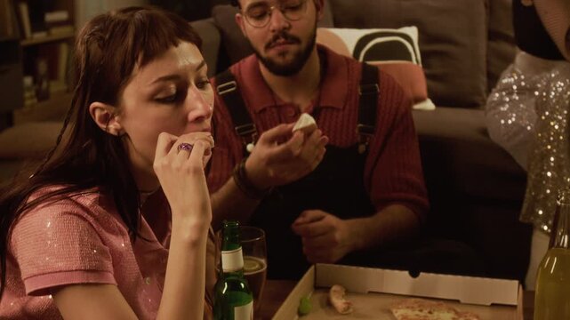 Tilt up shot of young adult woman sharing delivery food with male friend eating pizza and cheese while resting in living room after party