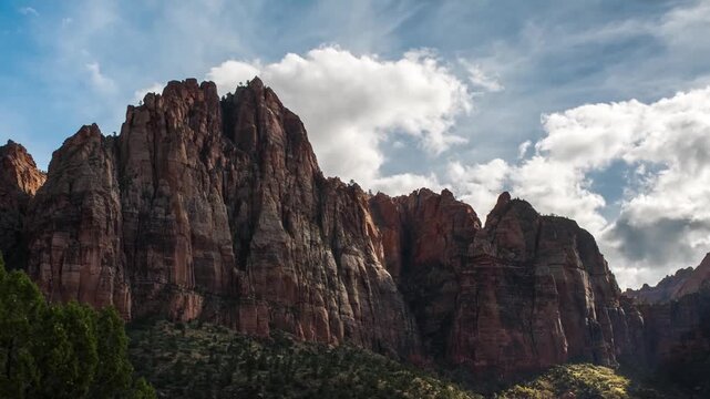 Scenic footage captures the towering Navajo sandstone cliffs and a dynamic, cloudy blue sky along the Sand Bench Trail in Zion National Park, Utah, USA. This trail is a popular area for guided horseba