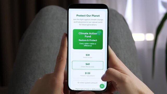 Supporting the planet through a smartphone app. Person selects a 60 dollars donation to fund forest protection and ocean cleaning. Essential footage for non-profit promos, climate change awareness