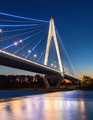 Fototapeta premium Stunning cable-stayed bridge illuminated at twilight, reflecting vibrant lights on the calm river below, showcasing modern architecture and urban beauty.