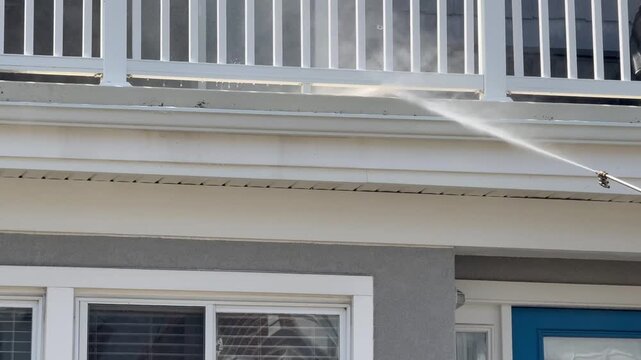 Power washing dirty front porch of a house with a spray nozzle shooting water and detergent