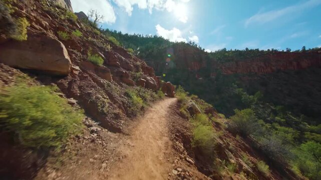 A first-person perspective shot while hiking the moderate Watchman Trail in Zion National Park, Utah. The dirt path winds through the canyon landscape, showcasing red rock formations, green vegetation