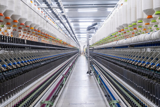 Balanced composition of spinning machines aligned in a textile factory corridor with central piping infrastructure.