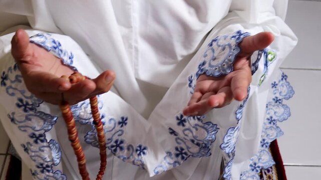 a Muslim woman is praying using a mukena and prayer beads