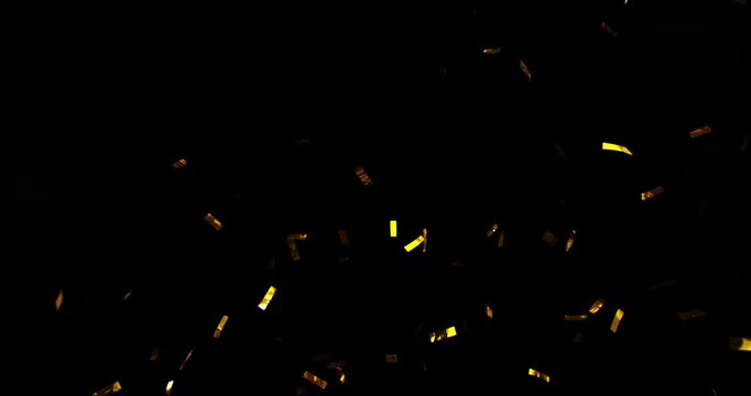 Golden confetti flying in super slow motion against a black background. Shiny metallic particles drifting and falling in the air, creating elegant festive atmosphere with dramatic lighting. Speed ramp