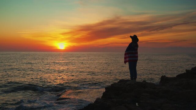 Woman holding American flag on ocean coast at sunset, symbol of freedom, independence and patriotism. Independence Day, America 250 celebration, national pride, travel lifestyle and empowerment themes