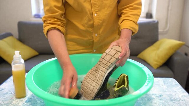 Cleaning sneakers using a soft brush and soap in a cozy indoor setting with a green bowl filled with water