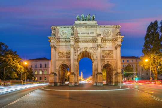Long exposure of the Siegestor triumphal arch in Munich, Germany, at twilight with vibrant traffic light trails.