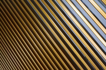Fototapeta premium Abstract close-up of a golden metal slat facade with diagonal lines and reflections, emphasizing texture, pattern, and architectural design, evoking modern and contemporary art.
