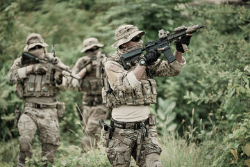 Obraz premium Military personnel in tactical gear advancing through dense vegetation