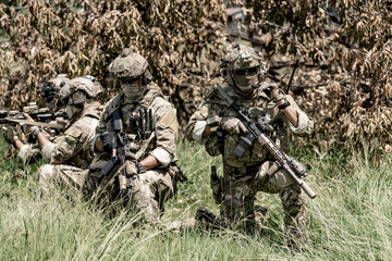 Fototapeta premium Special forces soldiers in camouflage gear with rifles in a grassy, wooded area