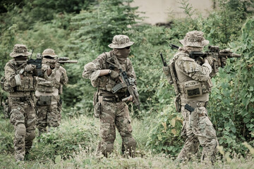 Fototapeta premium Special forces soldiers in camouflage gear advancing through dense foliage with rifles