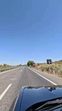 Vertical video of a car driving along a straight rural road on a sunny day, with clear blue skies, open road scenery, and a feeling of freedom